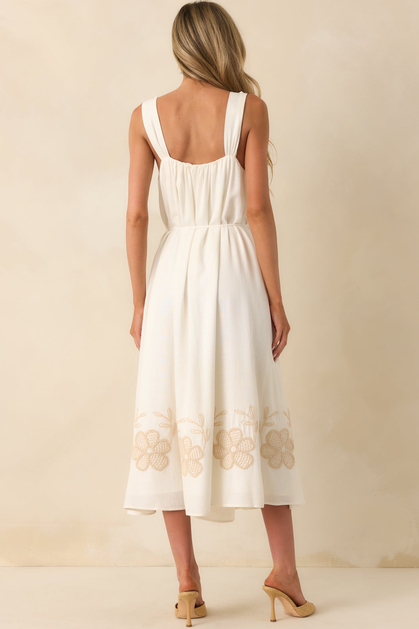 Rear view of the dress displaying the full length from behind, the gathered belt ties with petal tassels, and the continuation of the embroidered hem.