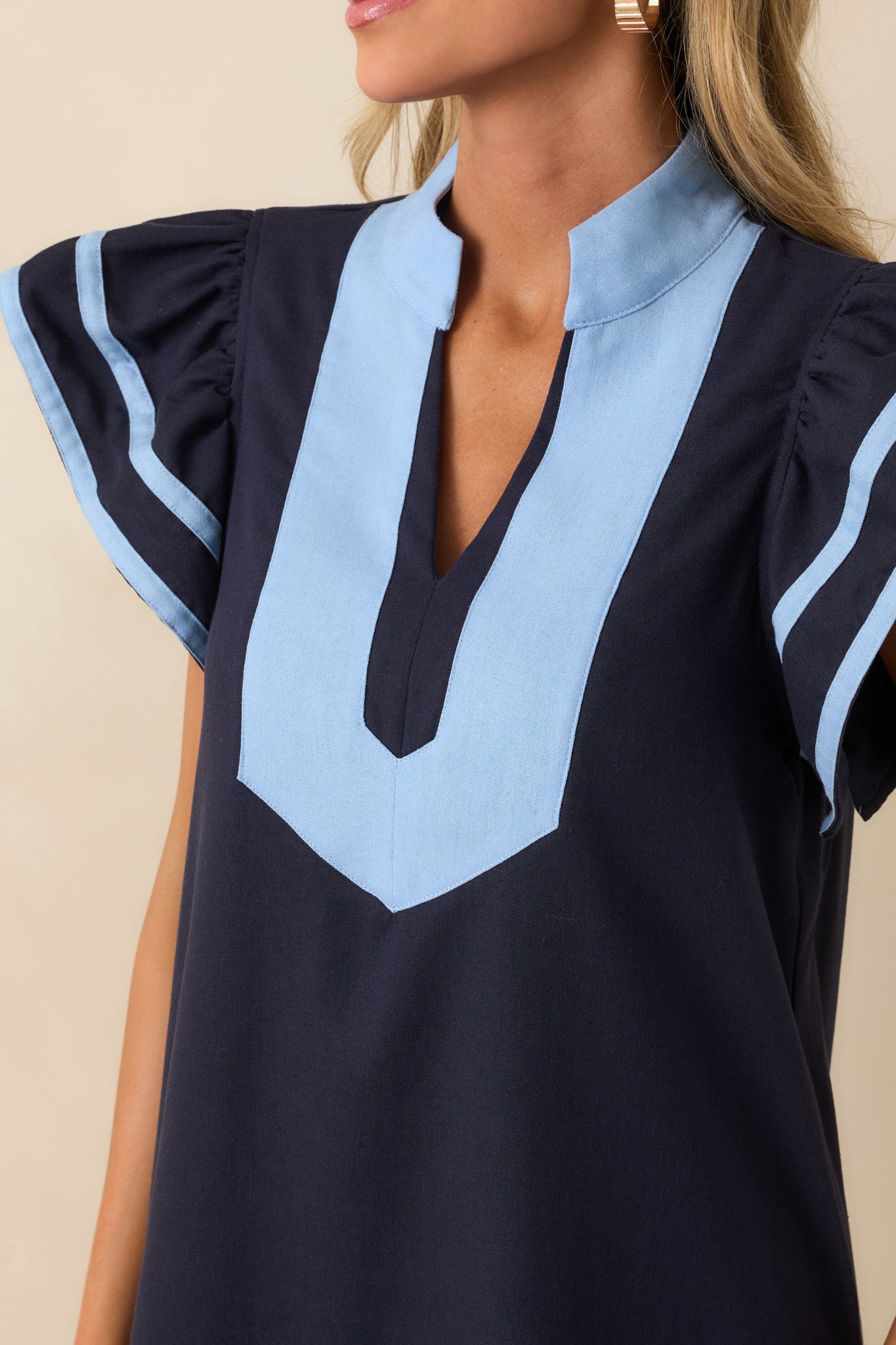 Tight view of the notch v-neckline and contrast trim, showing stitching details and the texture of the navy fabric.