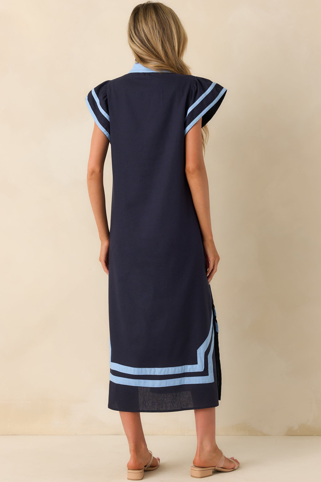 Rear view of the dress featuring the full navy back panel, flutter sleeve shape from behind, and subtle flare of the hemline with vent slits visible at the sides.