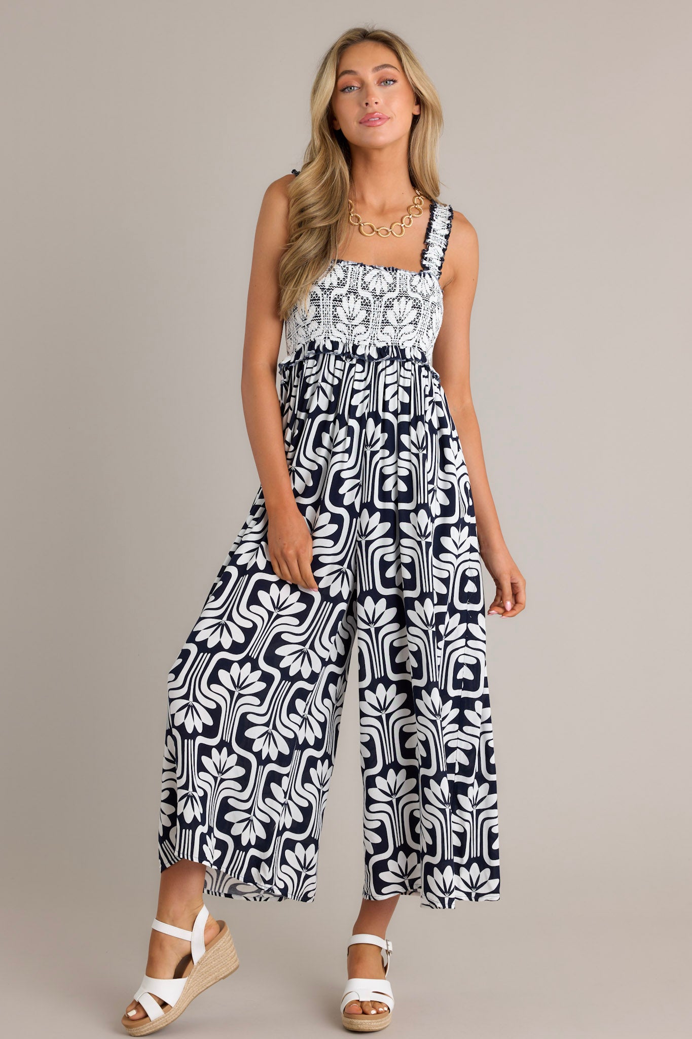 This black jumpsuit features a square neckline, elastic ruffle straps, a fully smocked bust, and a slightly cropped hemline.