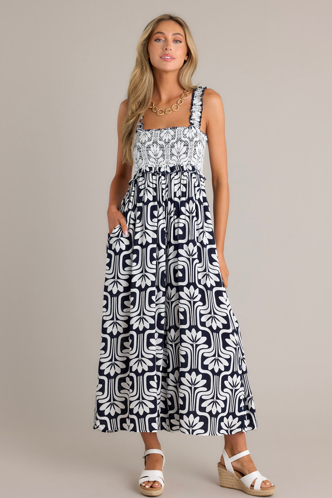 Angled Full length view of a black jumpsuit with a square neckline, elastic ruffle straps, a fully smocked bust, and a slightly cropped hemline