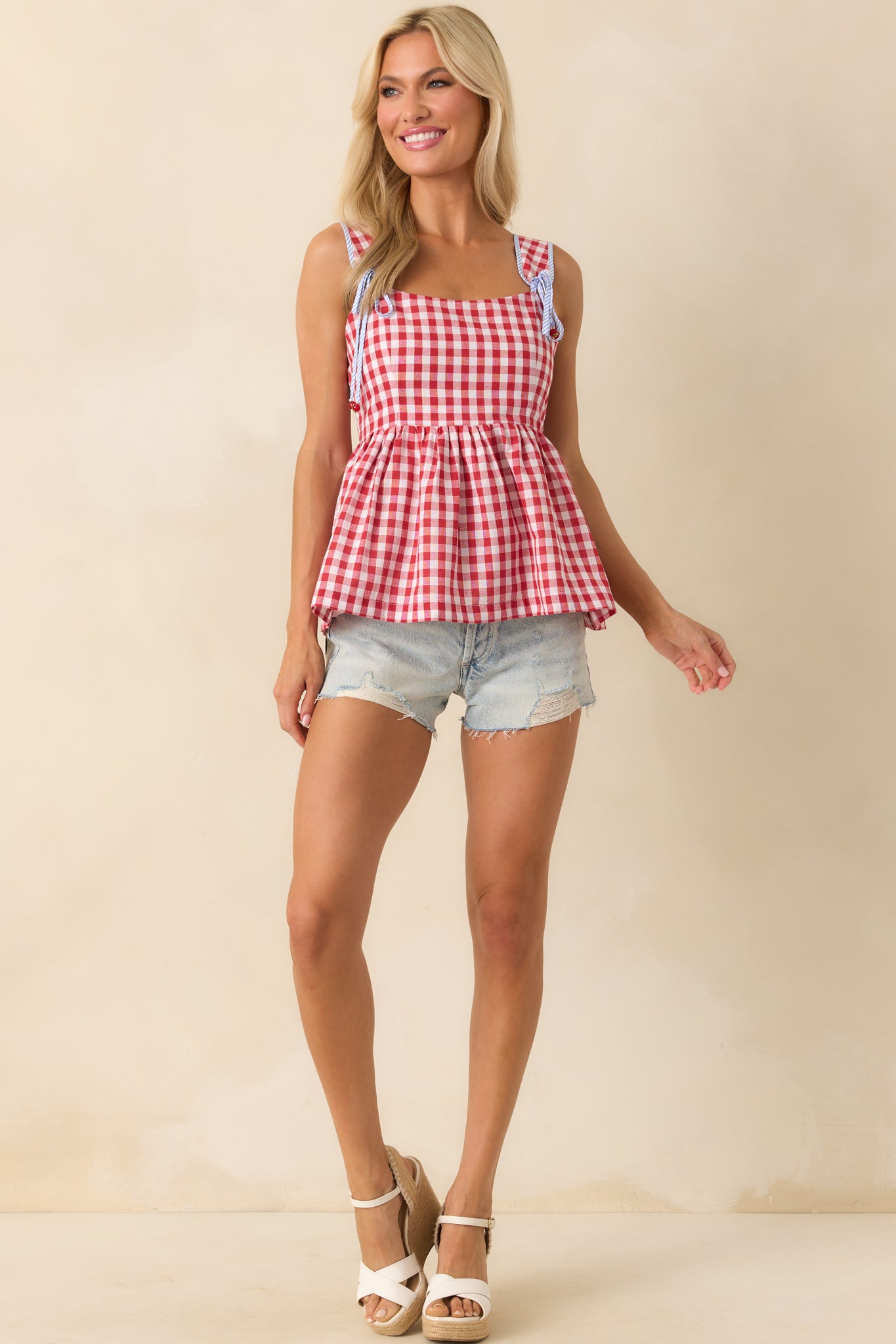 An angled full-body view showing the red gingham pattern, peplum silhouette, and striped bow straps with tomato charm ends.