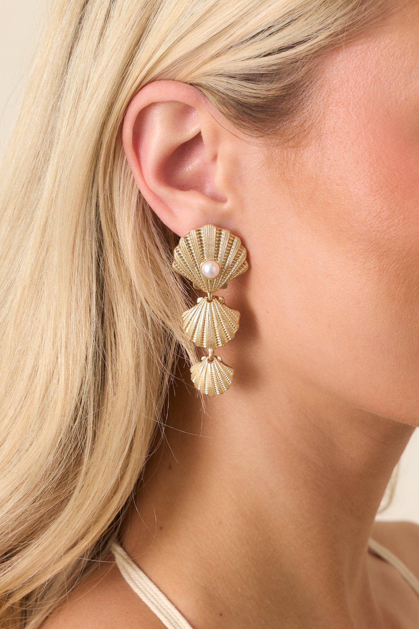 Close-up detail of earrings showing textured gold shell stud, pearl accent, and layered shell drops.