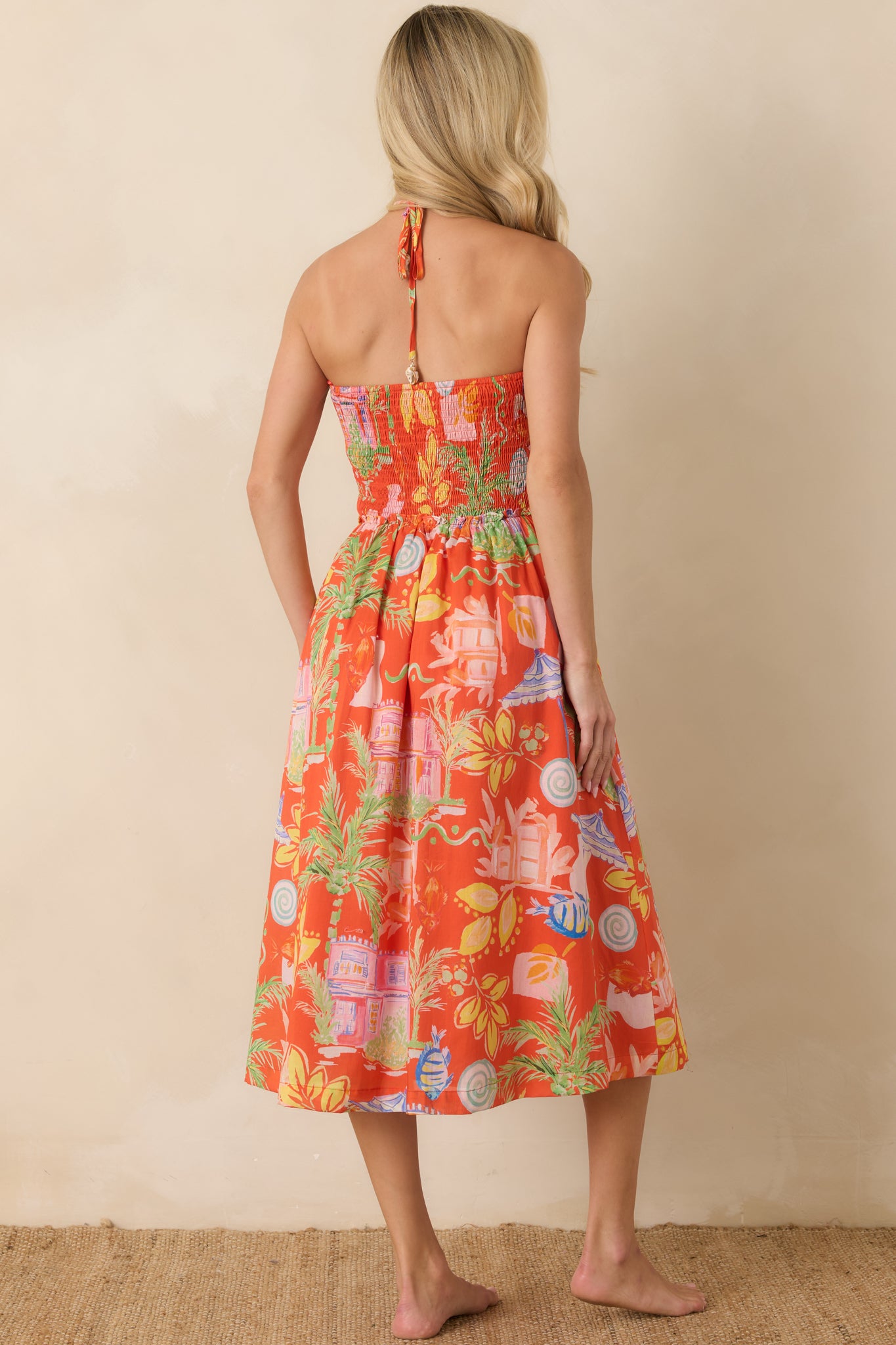 Rear view of the orange multi midi dress featuring a smocked back bodice, halter tie closure, and tiered flowing skirt.