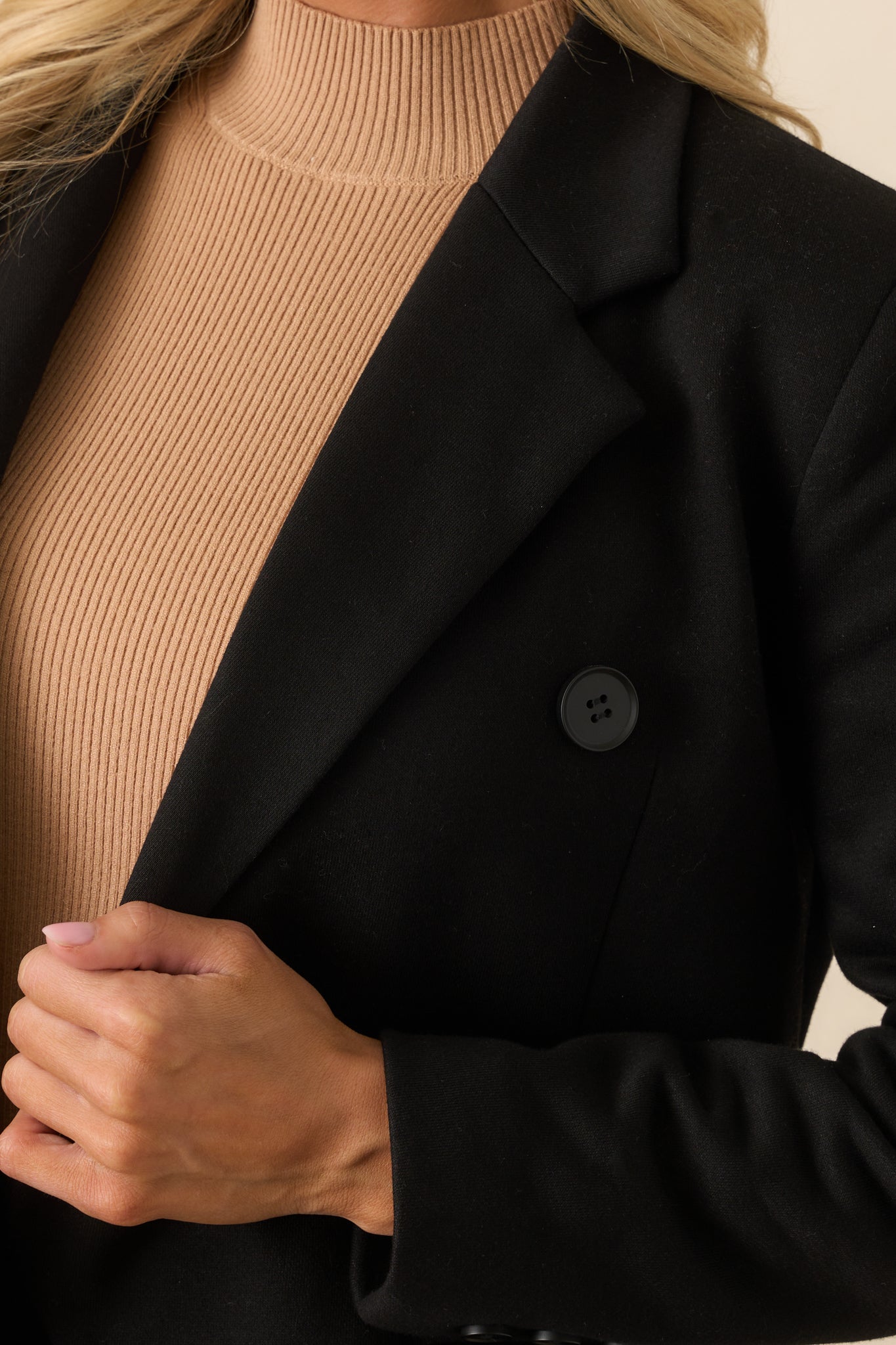 Close-up detail of a button and nearby stitching on the black blazer’s front closure.