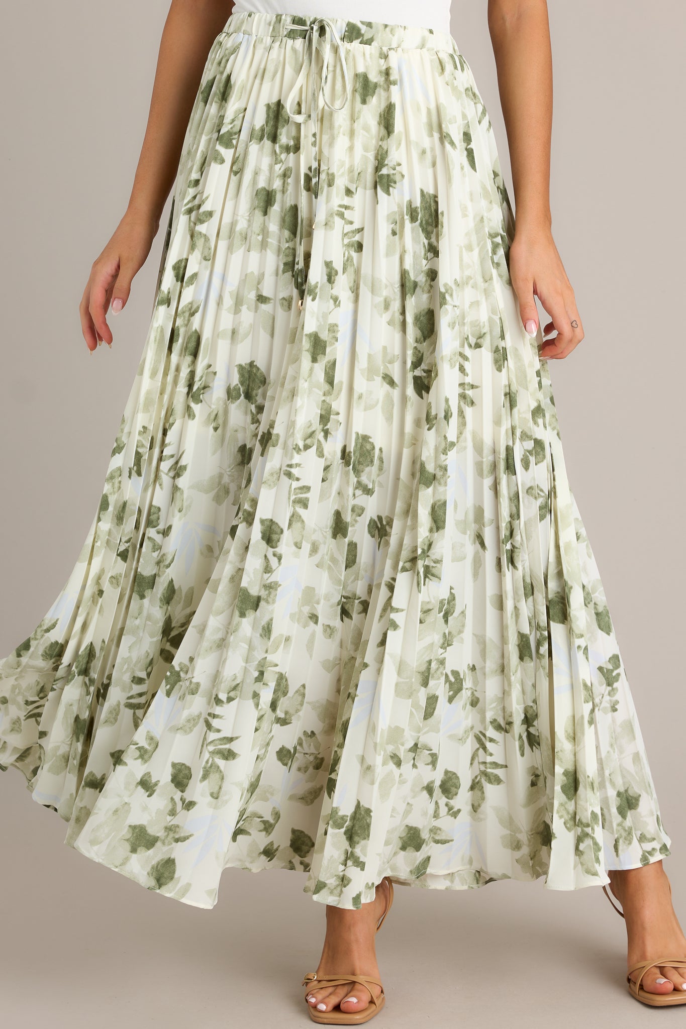Front view of a green skirt featuring a high waisted design, an elastic waistband, a self-tie drawstring with bead detailing, pleats throughout, and a flowing silhouette.