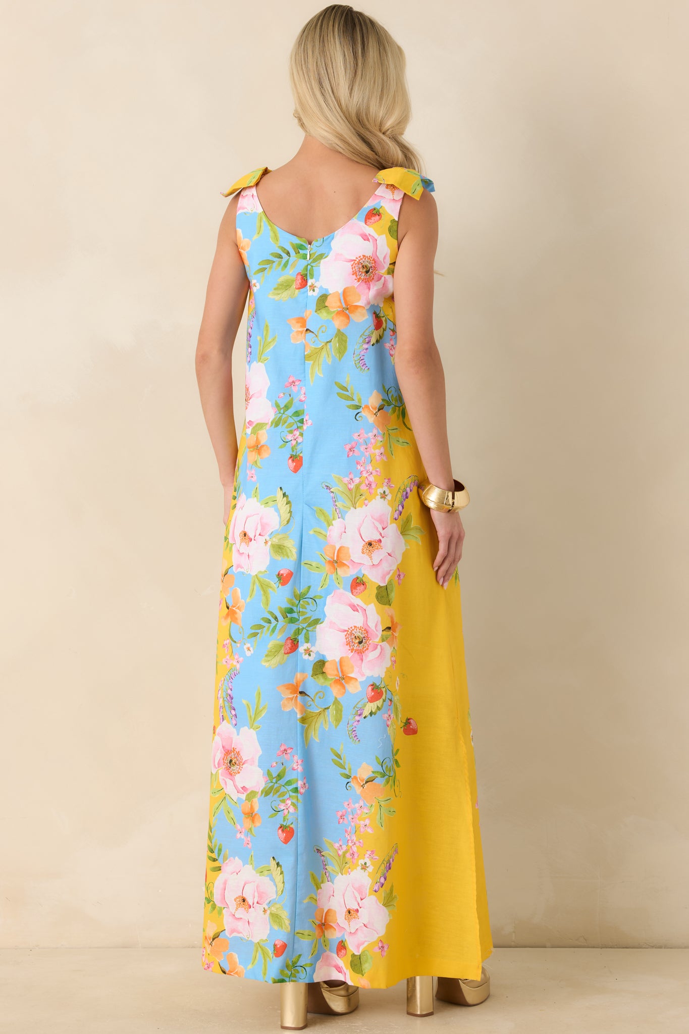 Rear view of the blue and yellow floral maxi dress featuring adjustable bow-tie straps, a relaxed silhouette, and a concealed zipper closure.