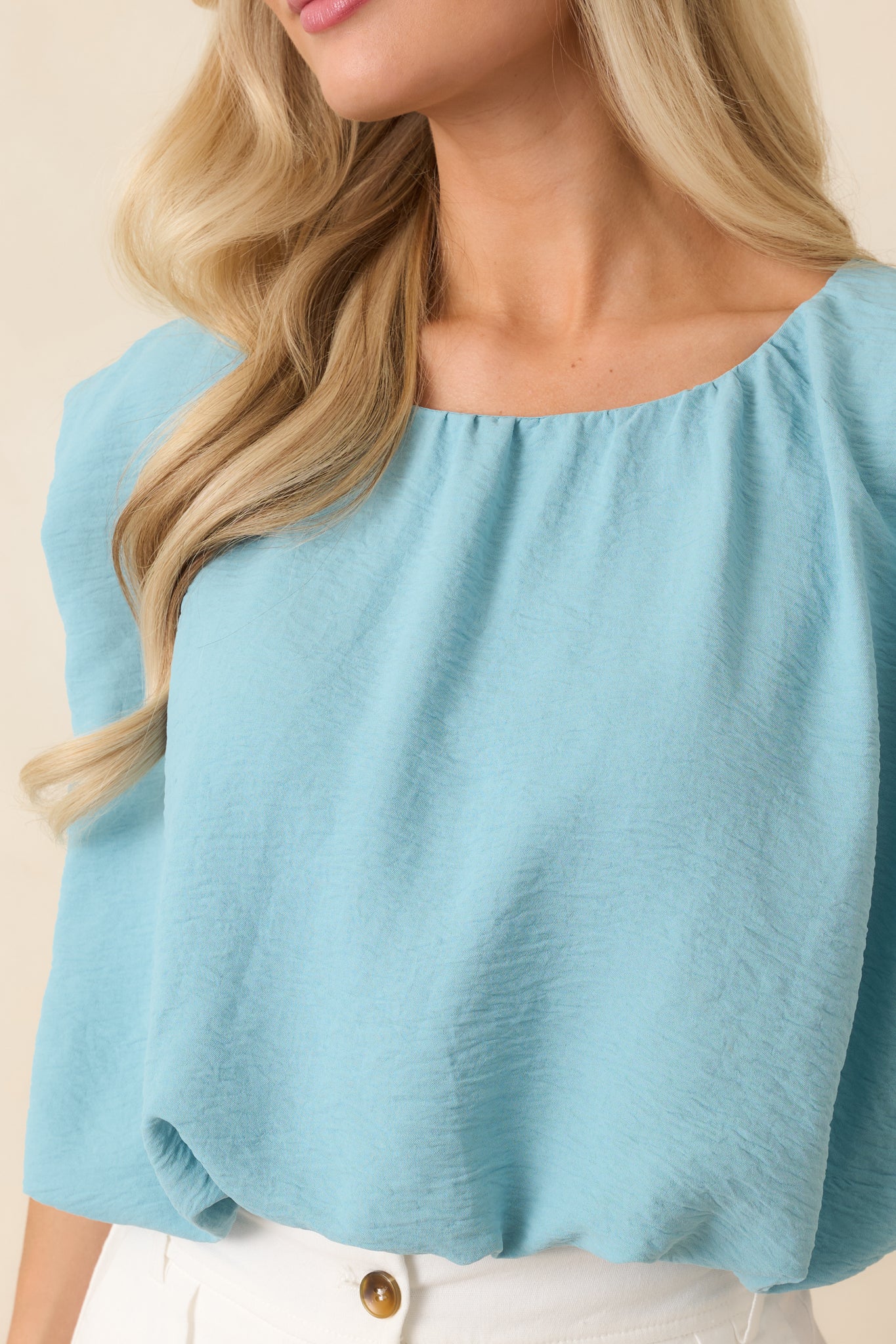 Close-up of the turquoise fabric featuring gathered neckline detailing, smooth construction, and elasticized hem accents.