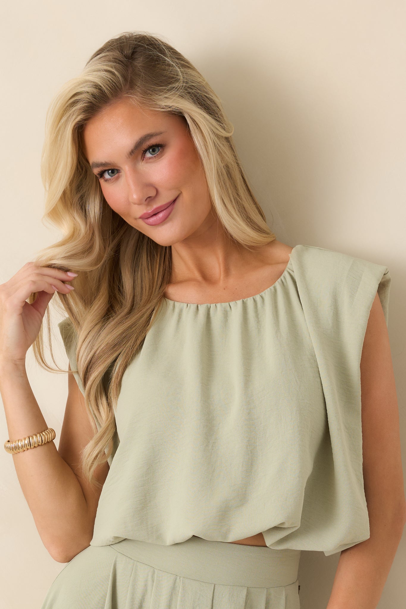 Elasticized hem detail on sage green blouson cropped top showing gathered structure.