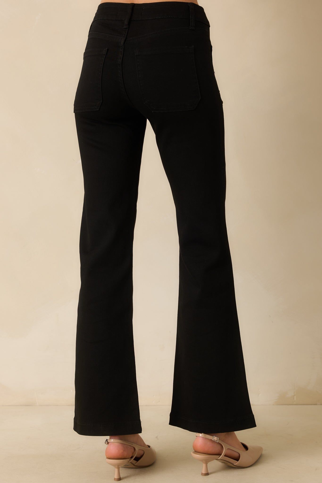 Rear view of black flare jeans highlighting back patch pockets, high-rise fit, and flared leg silhouette.