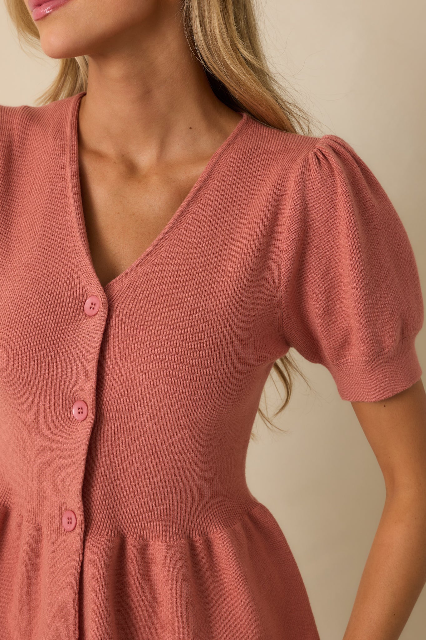 Close-up of the ribbed knit fabric, puff sleeves, and v-neckline of the rose pink top.