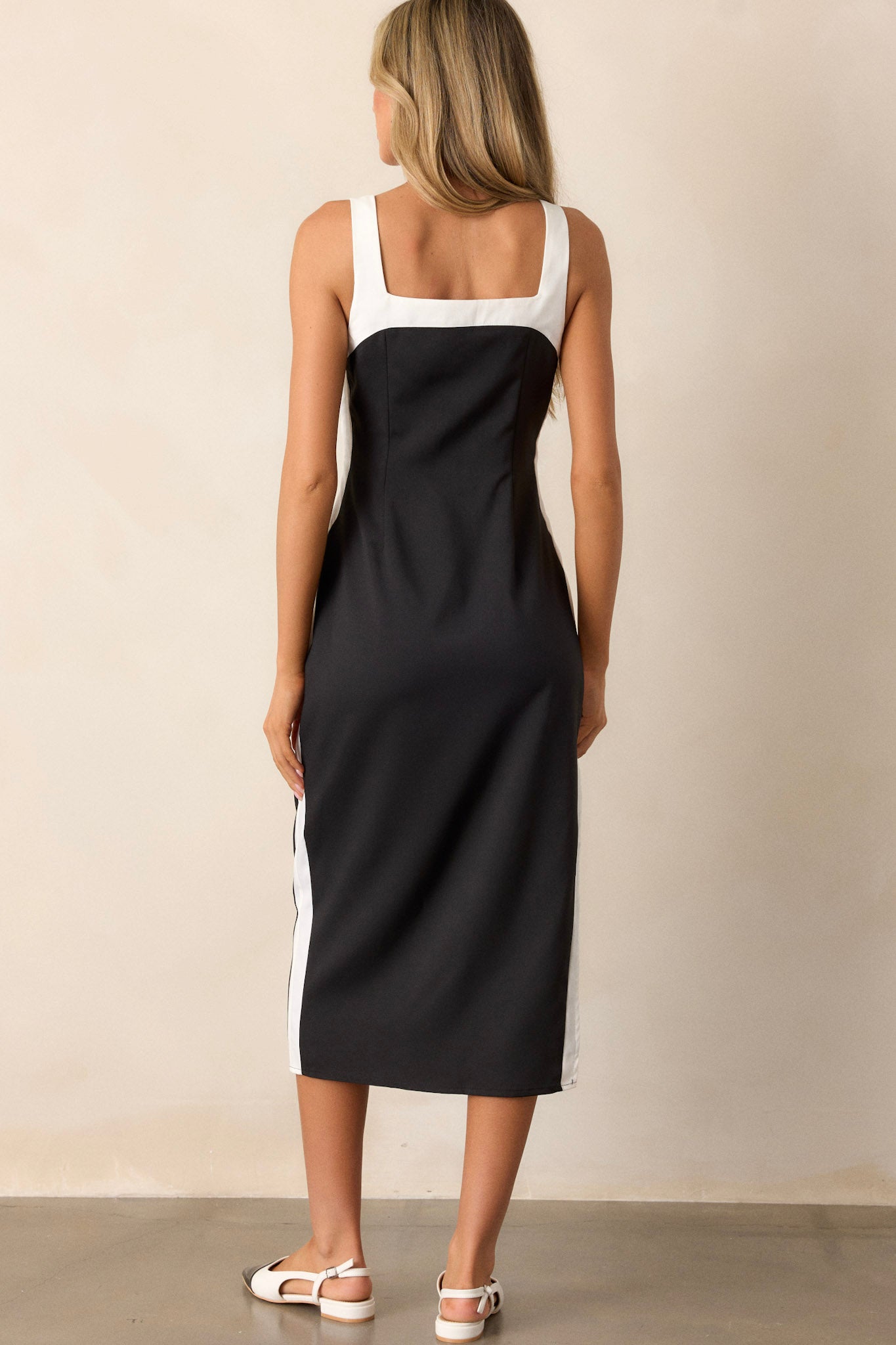 A view of the back of the black dress, showcasing the continuation of the white color-blocked trim and the fitted, streamlined design from behind.