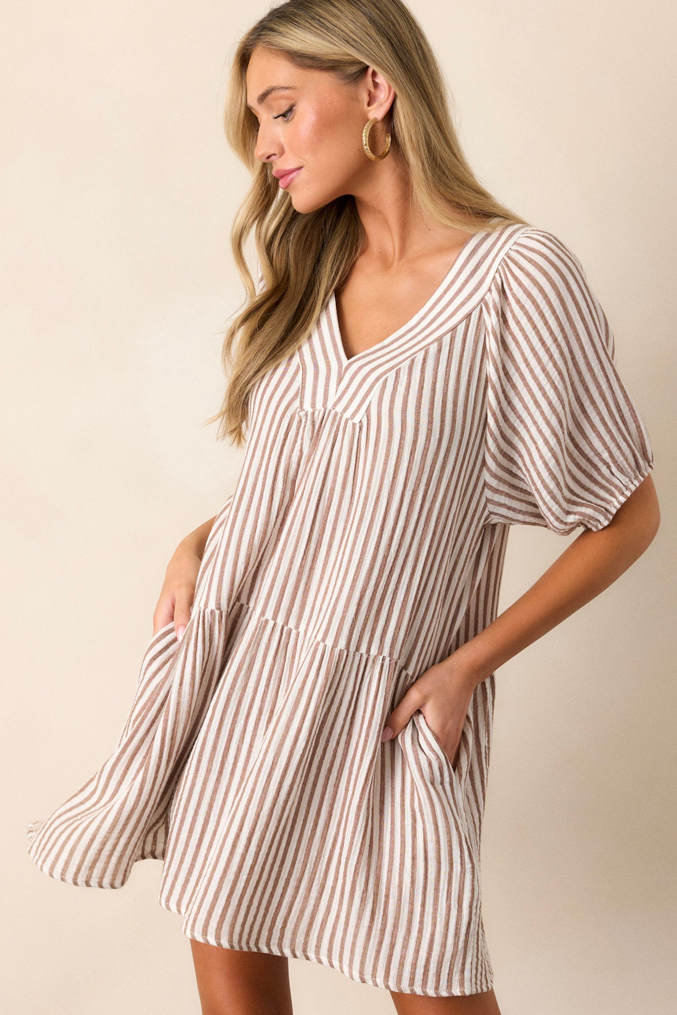 Side view of this brown stripe dress that features a thick v-neckline, a tiered design, a brown & ivory striped pattern, functional hip pockets, a light breathable fabric and elastic cuffed short sleeves.