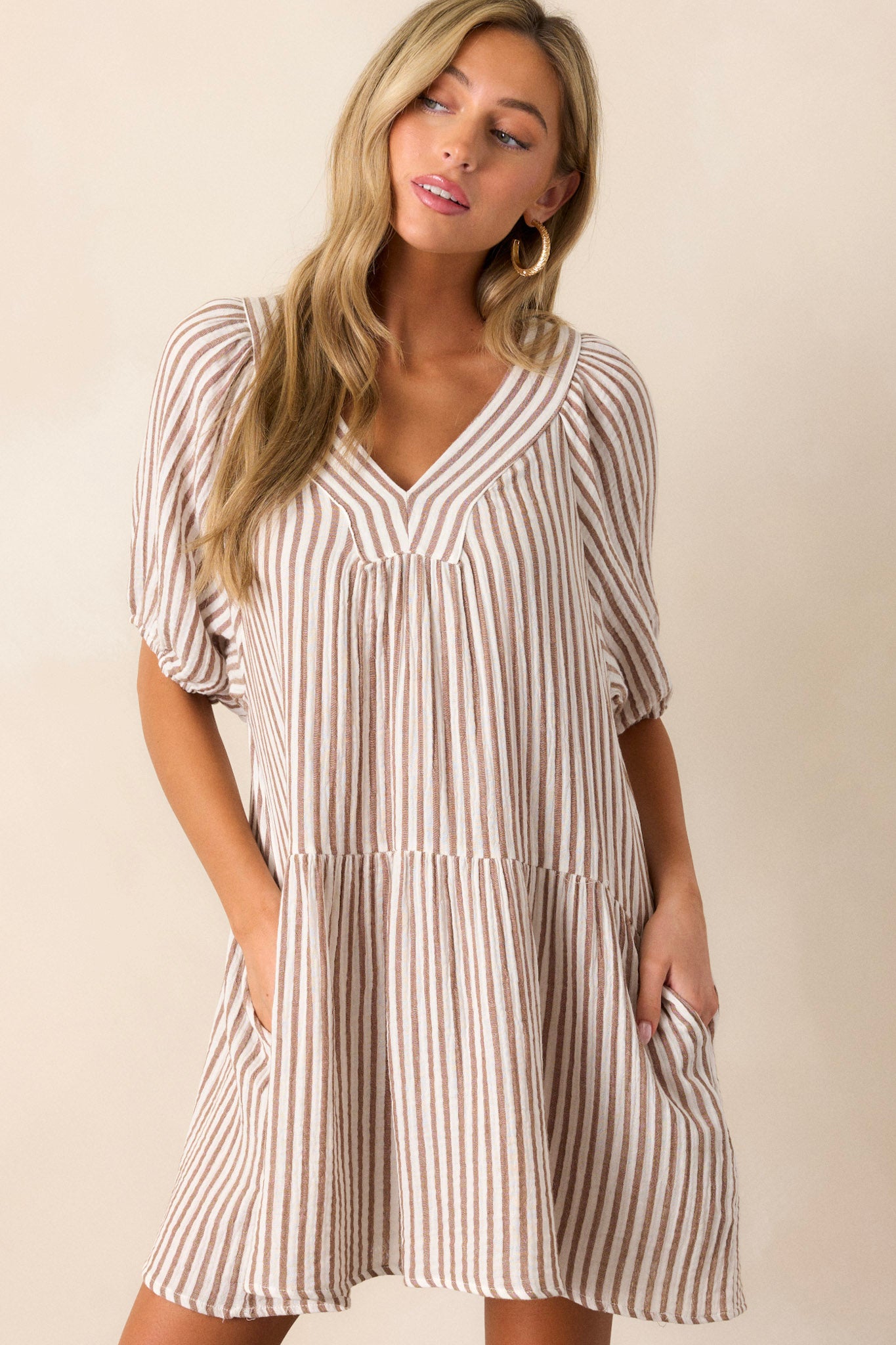 Front angled view of this brown stripe dress that features a thick v-neckline, a tiered design, a brown & ivory striped pattern, functional hip pockets, a light breathable fabric and elastic cuffed short sleeves.