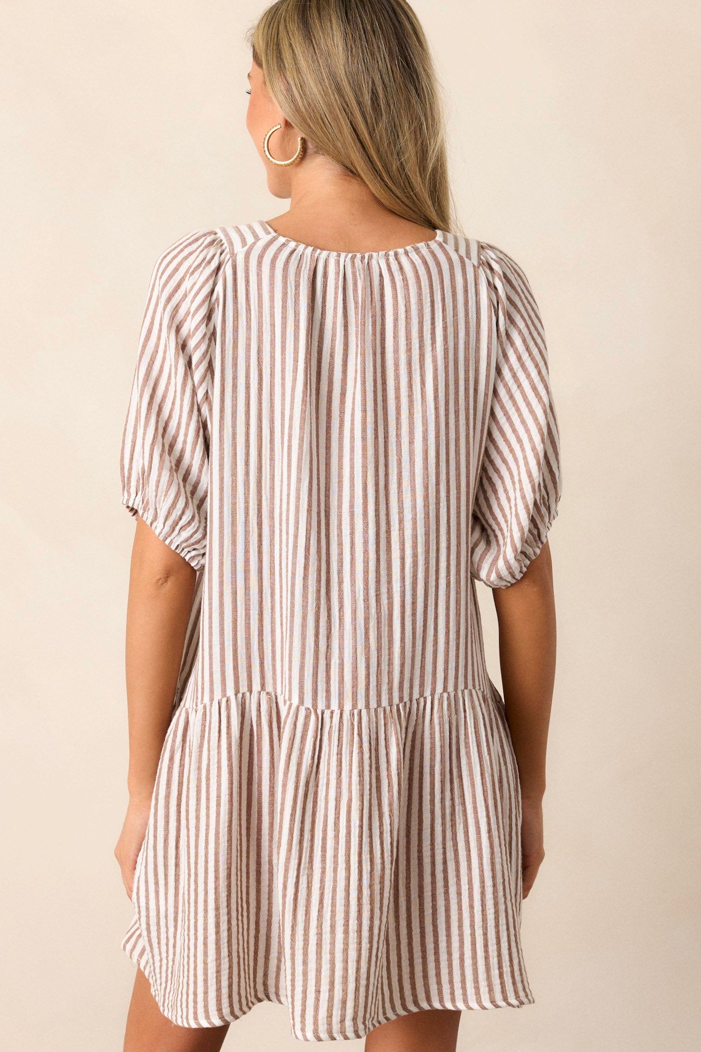 Back view of this brown stripe dress that features a thick v-neckline, a tiered design, a brown & ivory striped pattern, functional hip pockets, a light breathable fabric and elastic cuffed short sleeves.