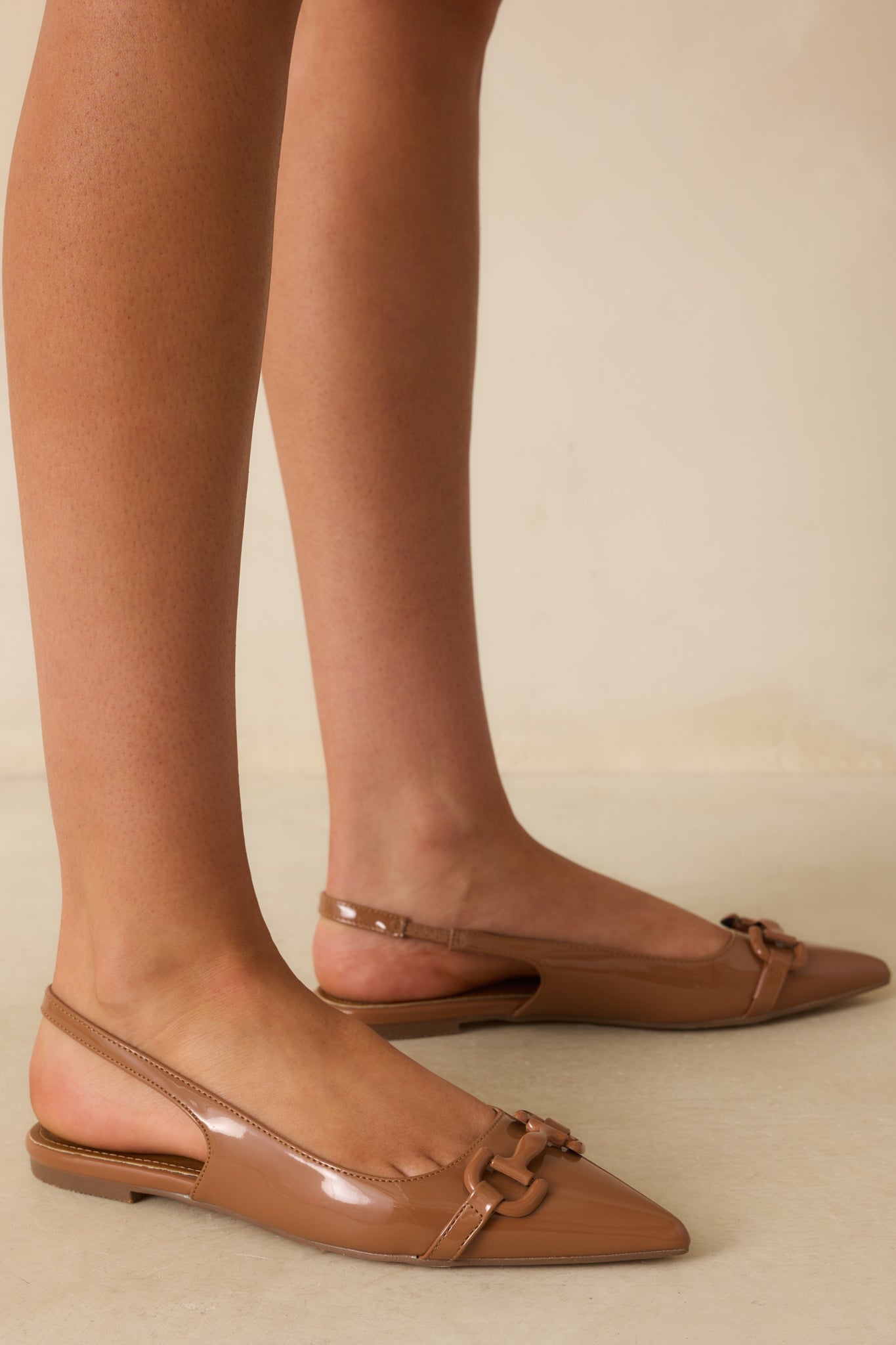 A cropped view of the mocha brown patent flats with a pointed toe and gold horsebit detail.