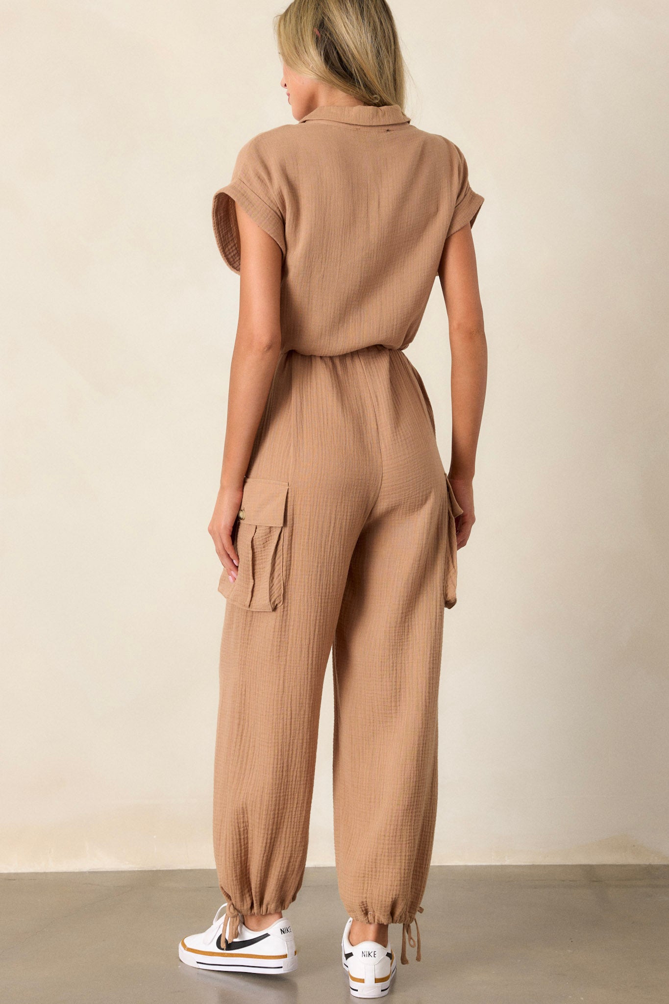 The jumpsuit shown from behind, featuring a plain back with visible seams, relaxed fit, cuffed short sleeves, and subtle shaping from the drawstring waist.