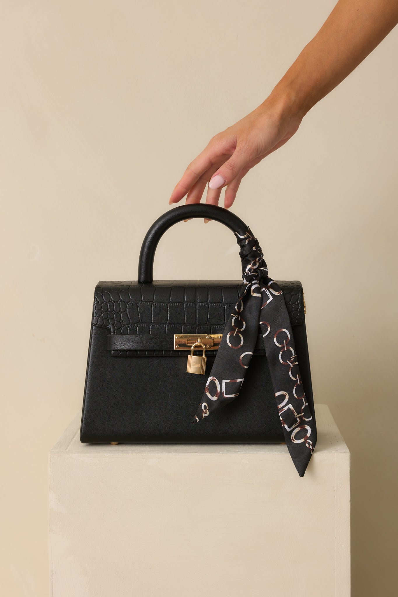 Full front photo of the black structured handbag with a removable faux croc leather flap and decorative self-tie bag scarf.