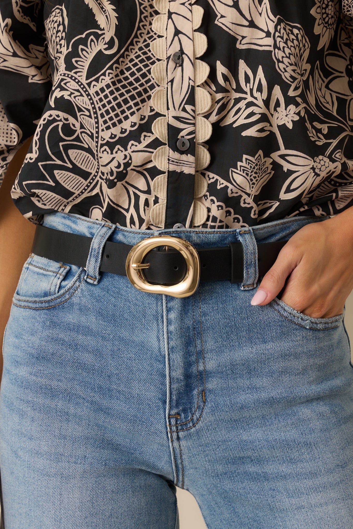 Close-up detail photo of the black belt focusing on the textured faux leather and unique organic-shaped gold buckle.