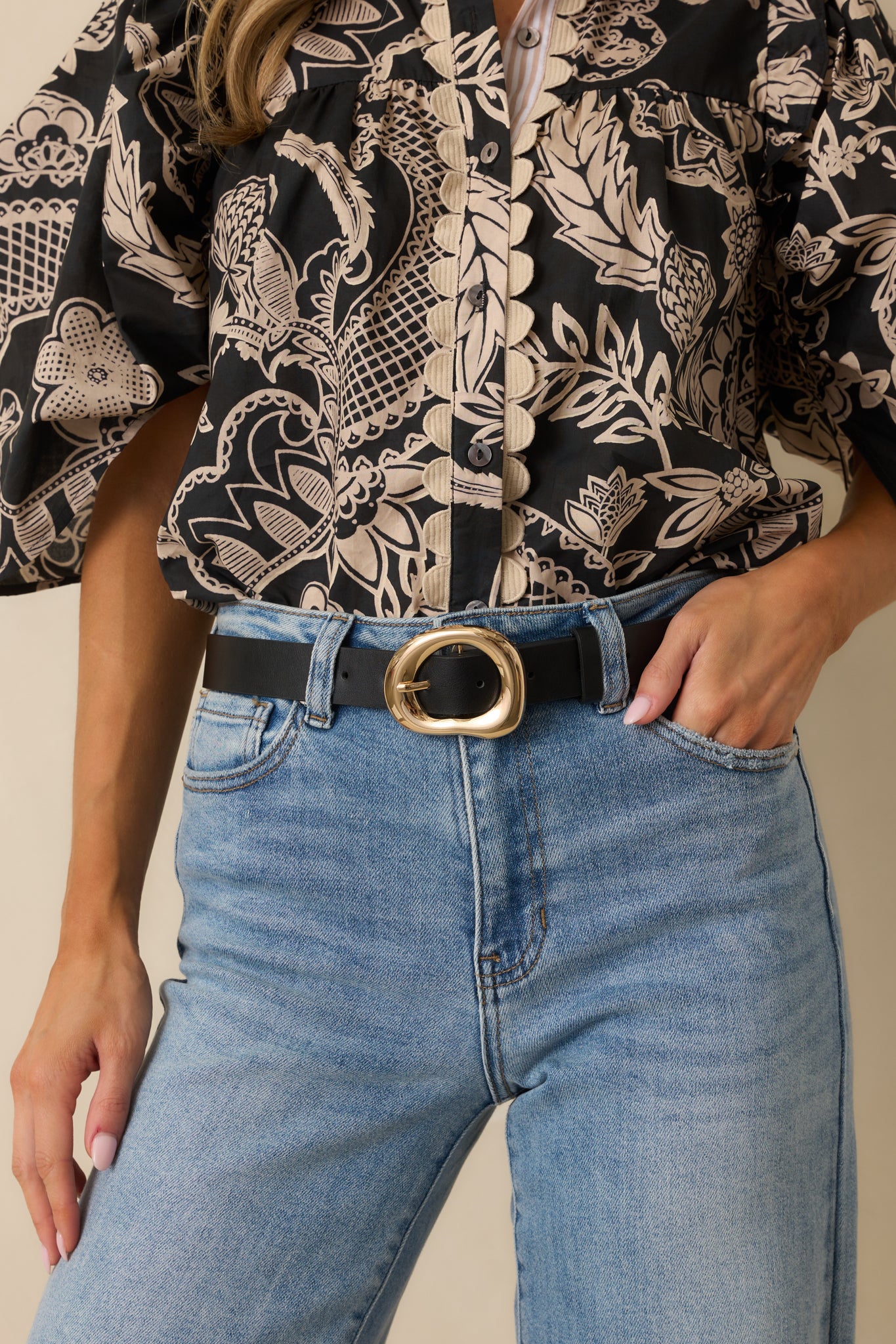 Cropped photo showing the black belt with smooth faux leather and a gold hollow organic-shaped buckle.