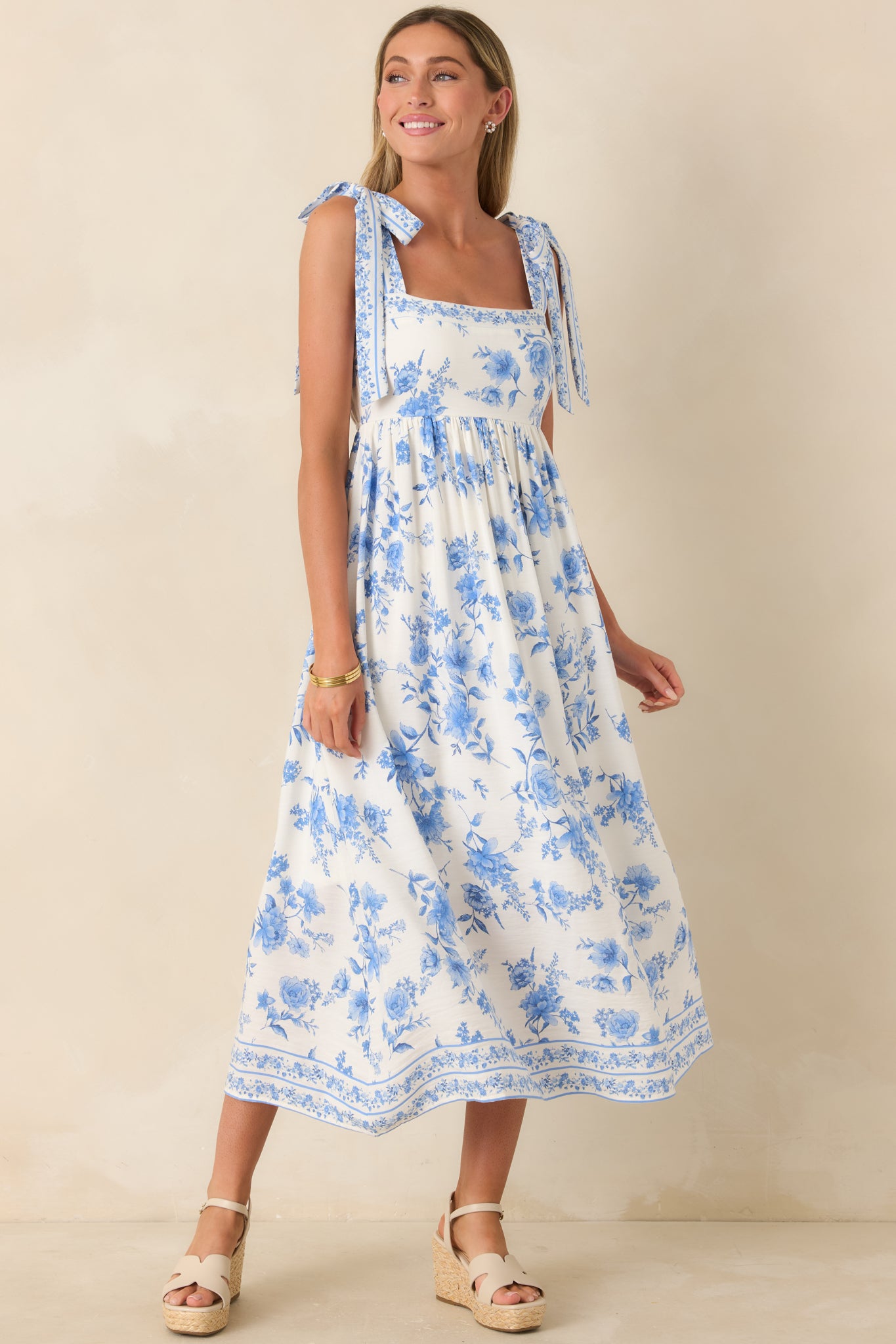 Ivory and blue floral maxi dress with adjustable tie straps, a structured bodice, softly gathered skirt, and a border print hem flowing through the maxi-length silhouette.