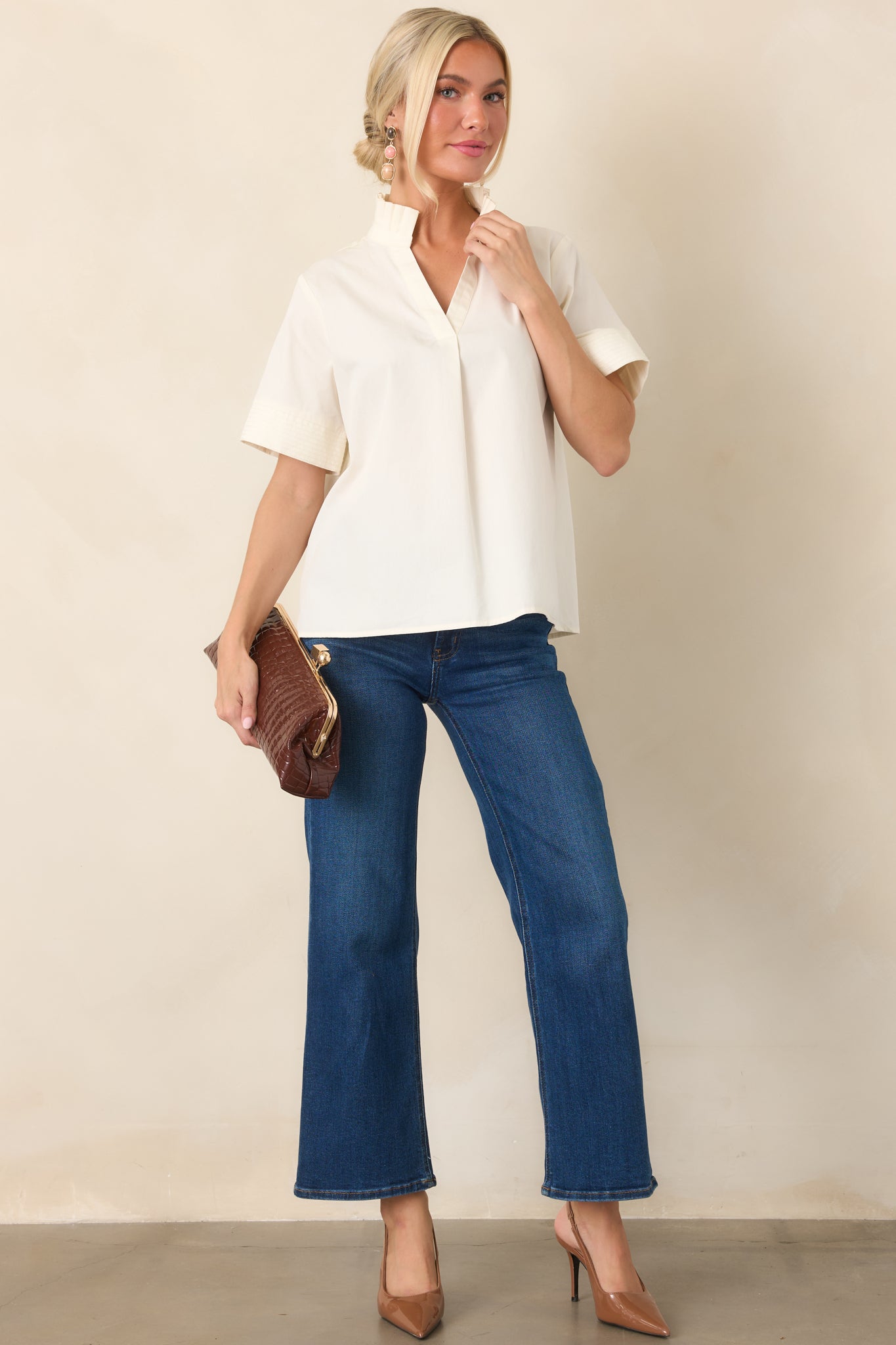 Ivory cotton top featuring a pleated ruffle collar, split neckline, short sleeves, and stitched cuff details, styled with a relaxed, polished silhouette.