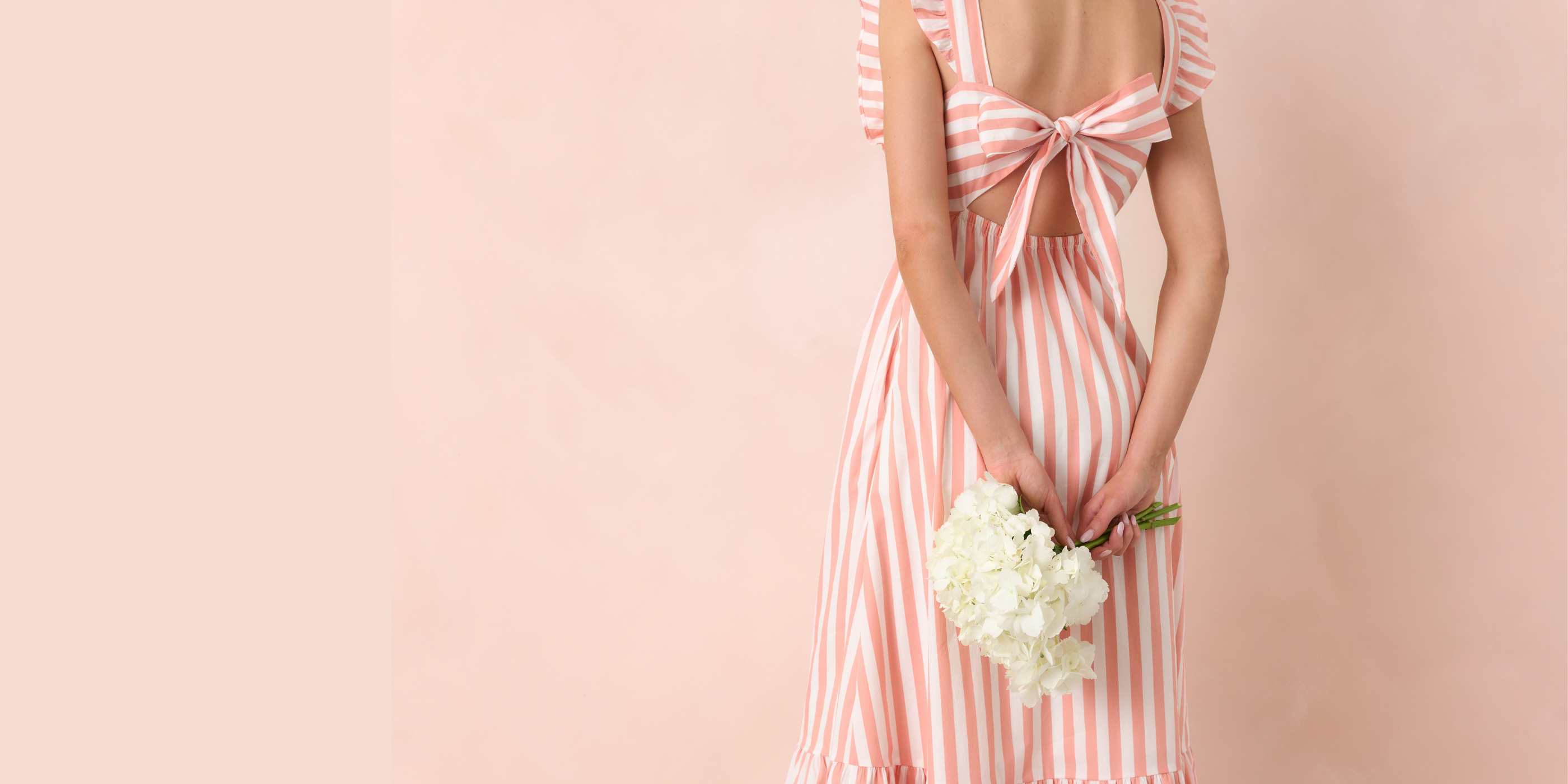 Woman in a pink and white striped dress holding flowers against a light pink background