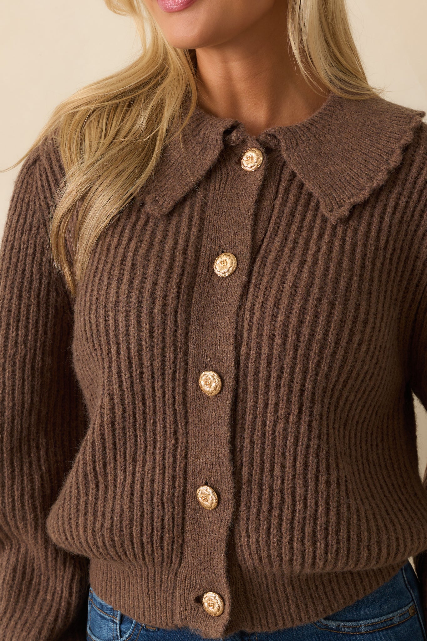 Detailed shot of ribbed knit fabric, scalloped peter pan collar, and gold embossed buttons.