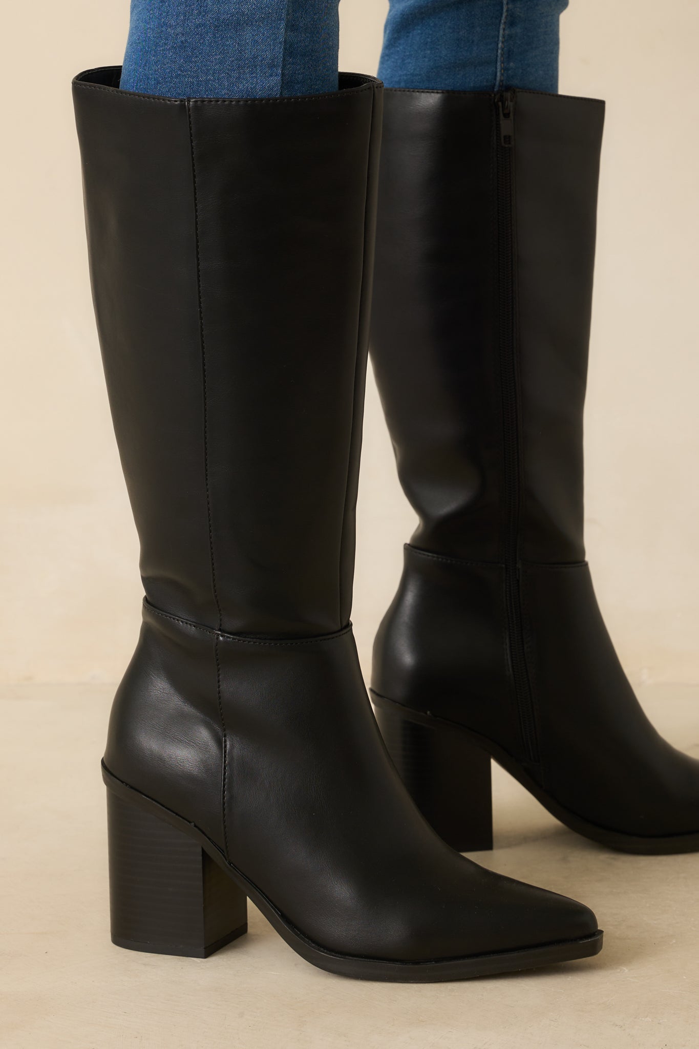 Side view showing the zipper closure, paneled design, and silhouette of black faux leather boots.