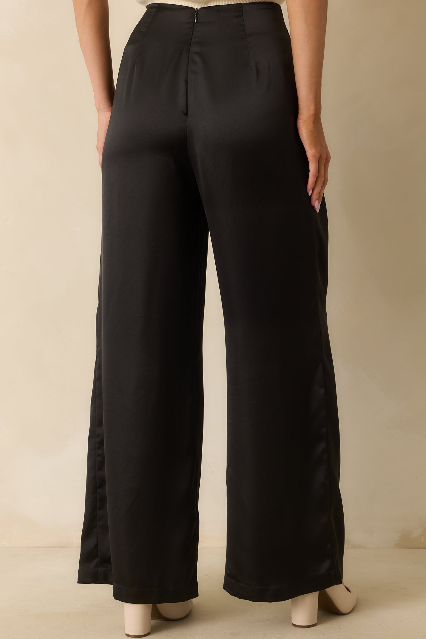 Rear view of black satin pants featuring a discrete back zipper and full-length wide legs.