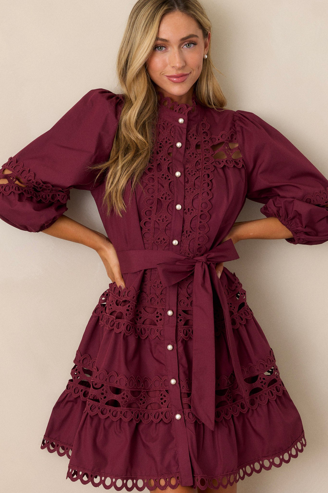 Font view of this plum mini dress featuring a high neckline, a functional button front with faux pearl buttons, an optional self-tie belt, elastic cuffed 3/4 length sleeves, and eyelet detailing throughout.