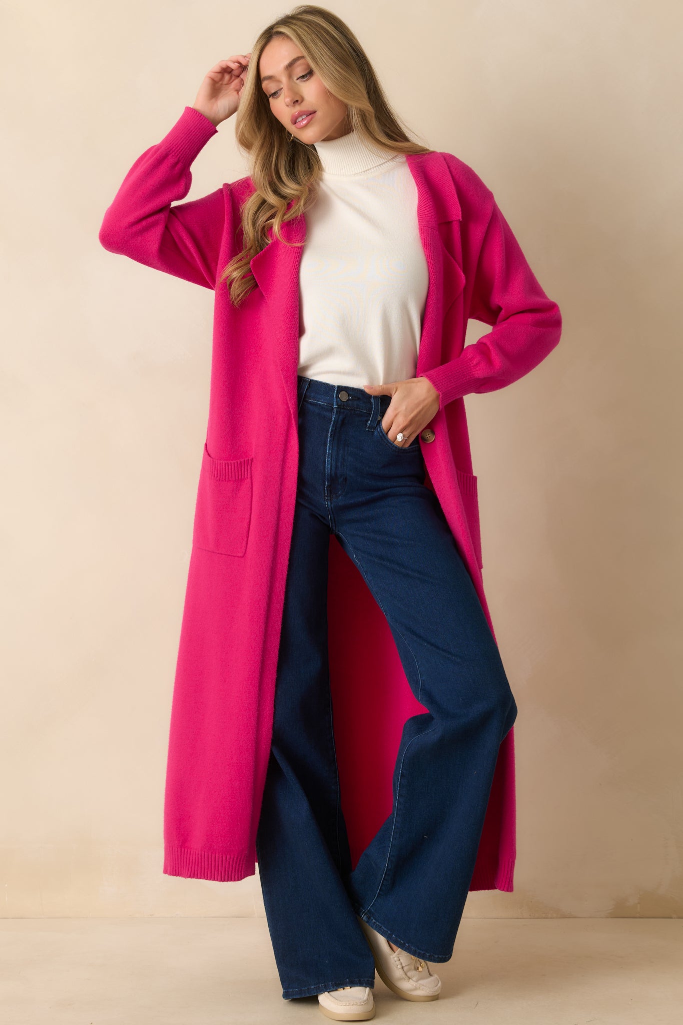 Full front view of the hot pink cardigan showing the longline cut, single button closure, and functional pockets.