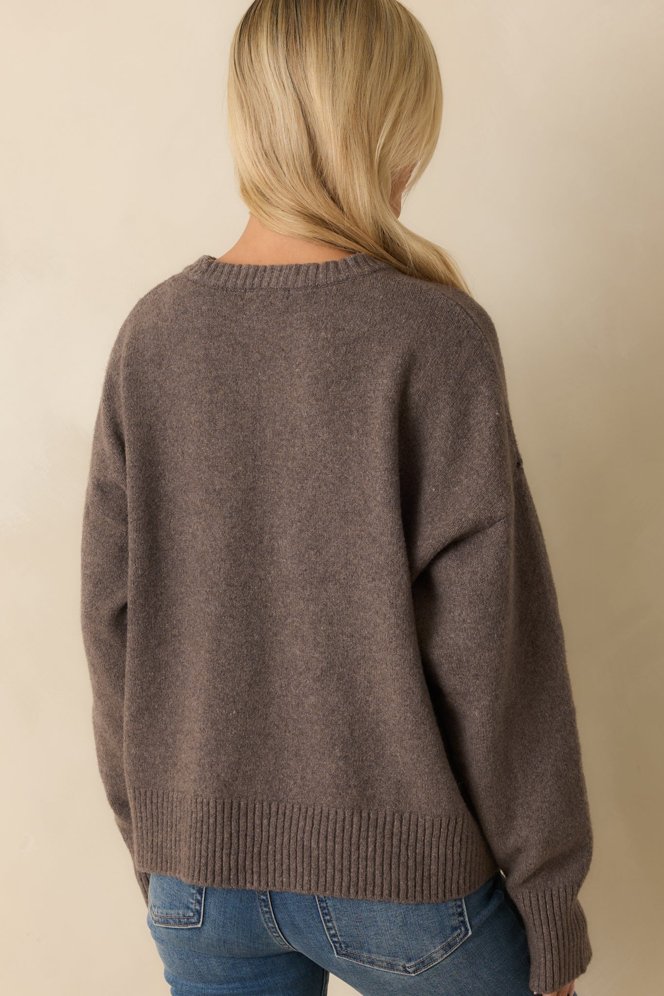 Rear view of the ash grey sweater showing the long sleeves, relaxed silhouette, and ribbed hem finish.