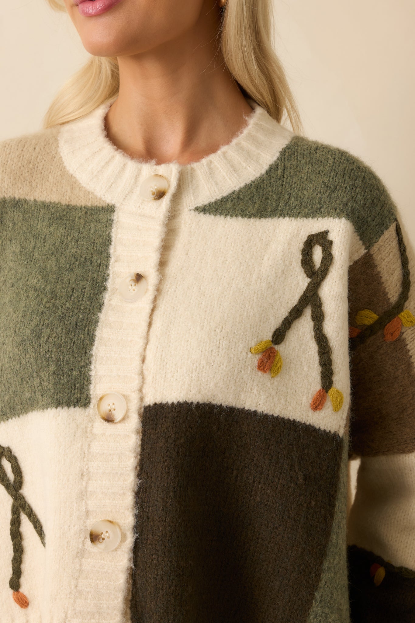 A close-up detail of the ivory cardigan showing raised floral embroidery and ribbed knit texture.