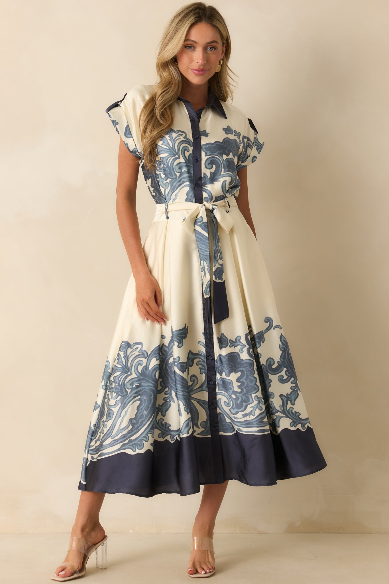 Front view of ivory maxi dress featuring navy baroque-inspired border print, collared neckline, cuffed short sleeves, optional sash belt, and flowing skirt.