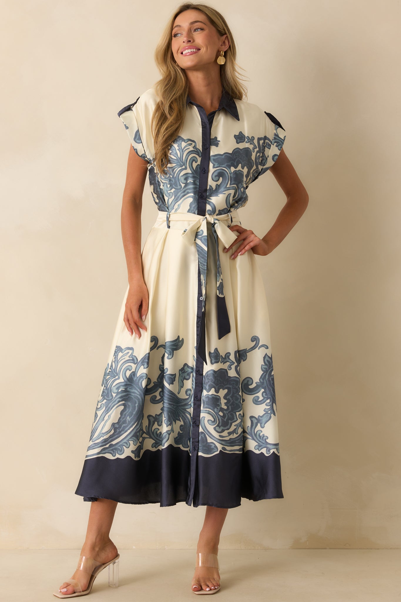 Ivory maxi dress with wide flowing skirt, optional sash tied at the waist, and baroque-inspired print accenting the bottom.