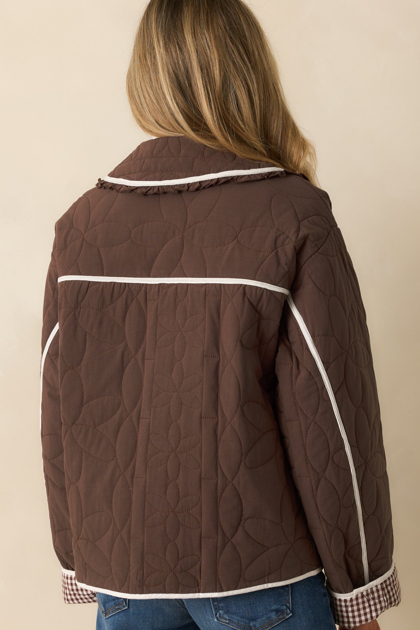 Rear view of the brown quilted jacket with smooth back, long sleeves, and subtle floral stitching.