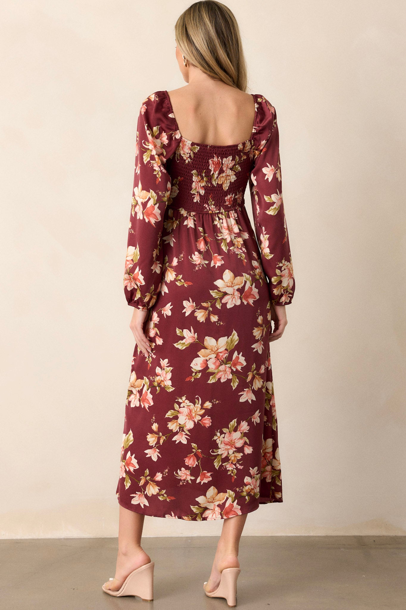 Back view of the burgundy floral dress, displaying the smocked back insert, elastic cuffed long sleeves, and the overall elegant silhouette from behind.