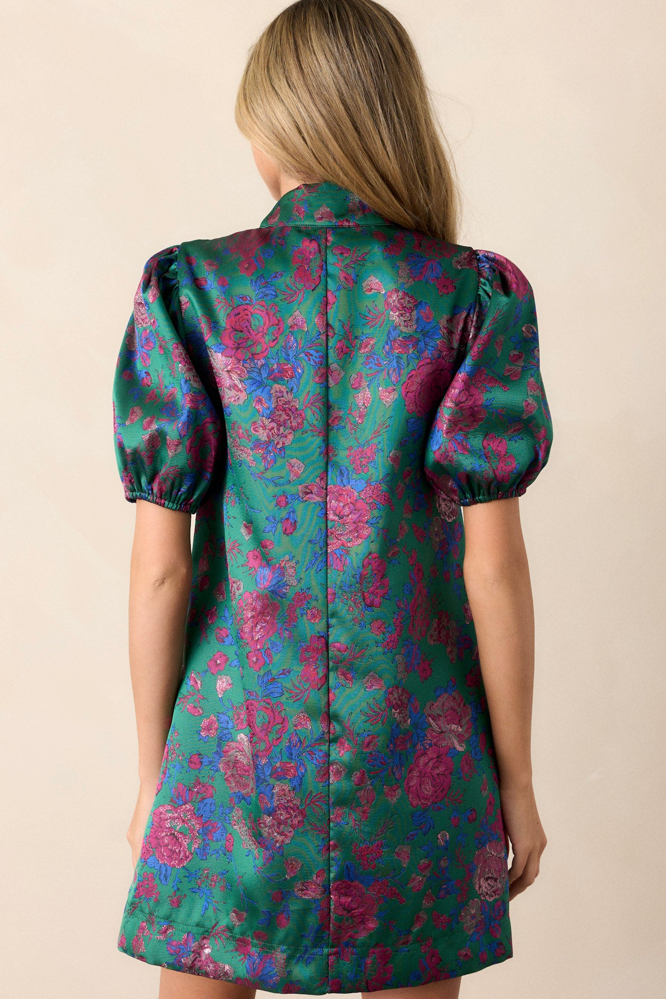 Back view of this green dress that features a tie-neckline, elastic puff sleeves, multi-color jacquard fabric, and a mini length.