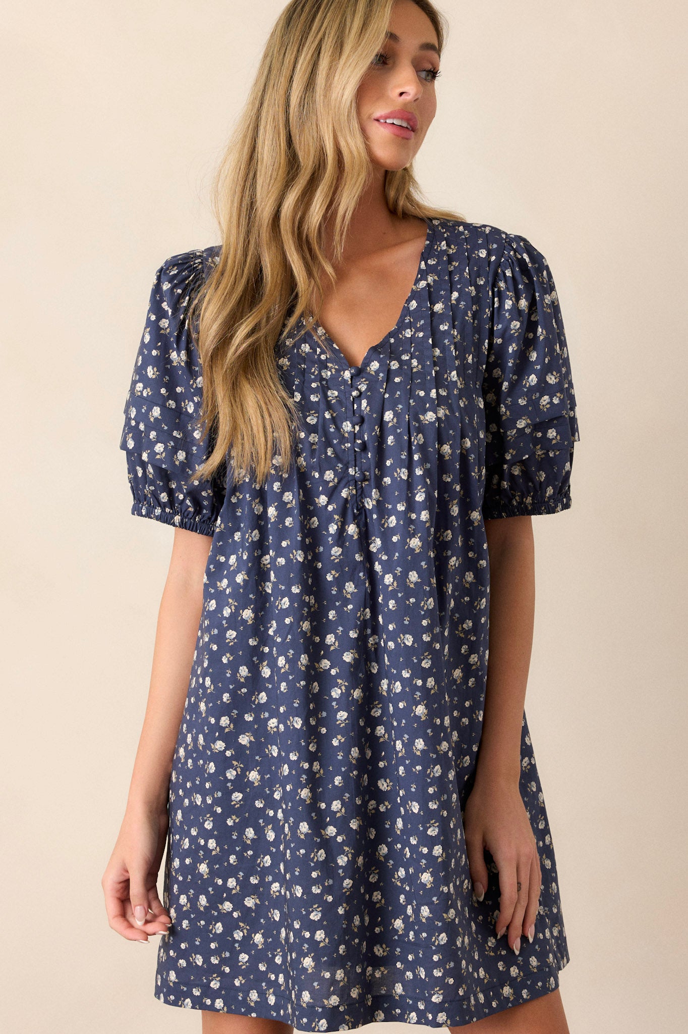 Front view of this navy dress that features a v-neckline, pleats in the bust, a relaxed fit, a floral pattern and short puff sleeves.