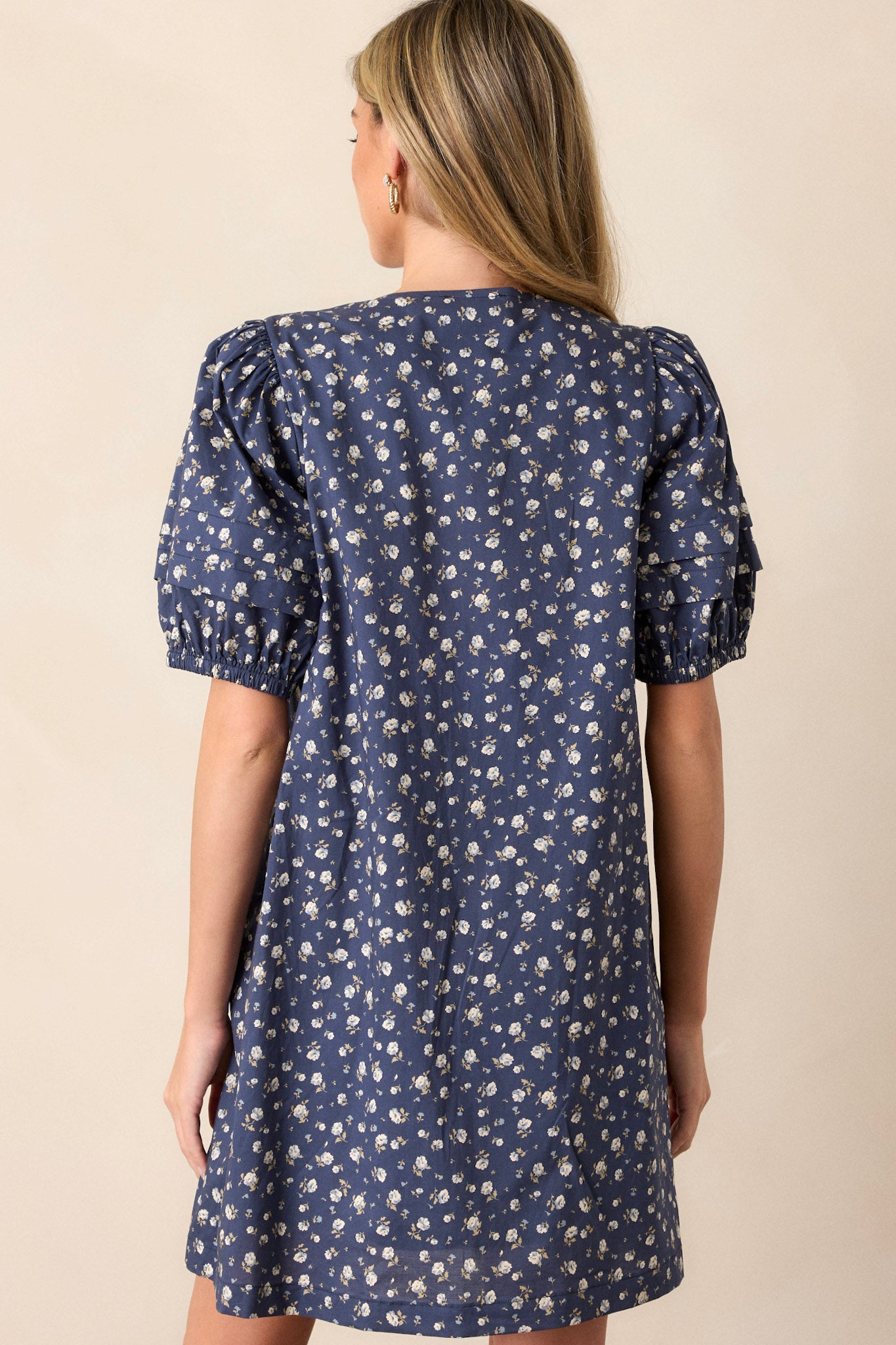 Back view of this navy dress that features a v-neckline, pleats in the bust, a relaxed fit, a floral pattern and short puff sleeves.