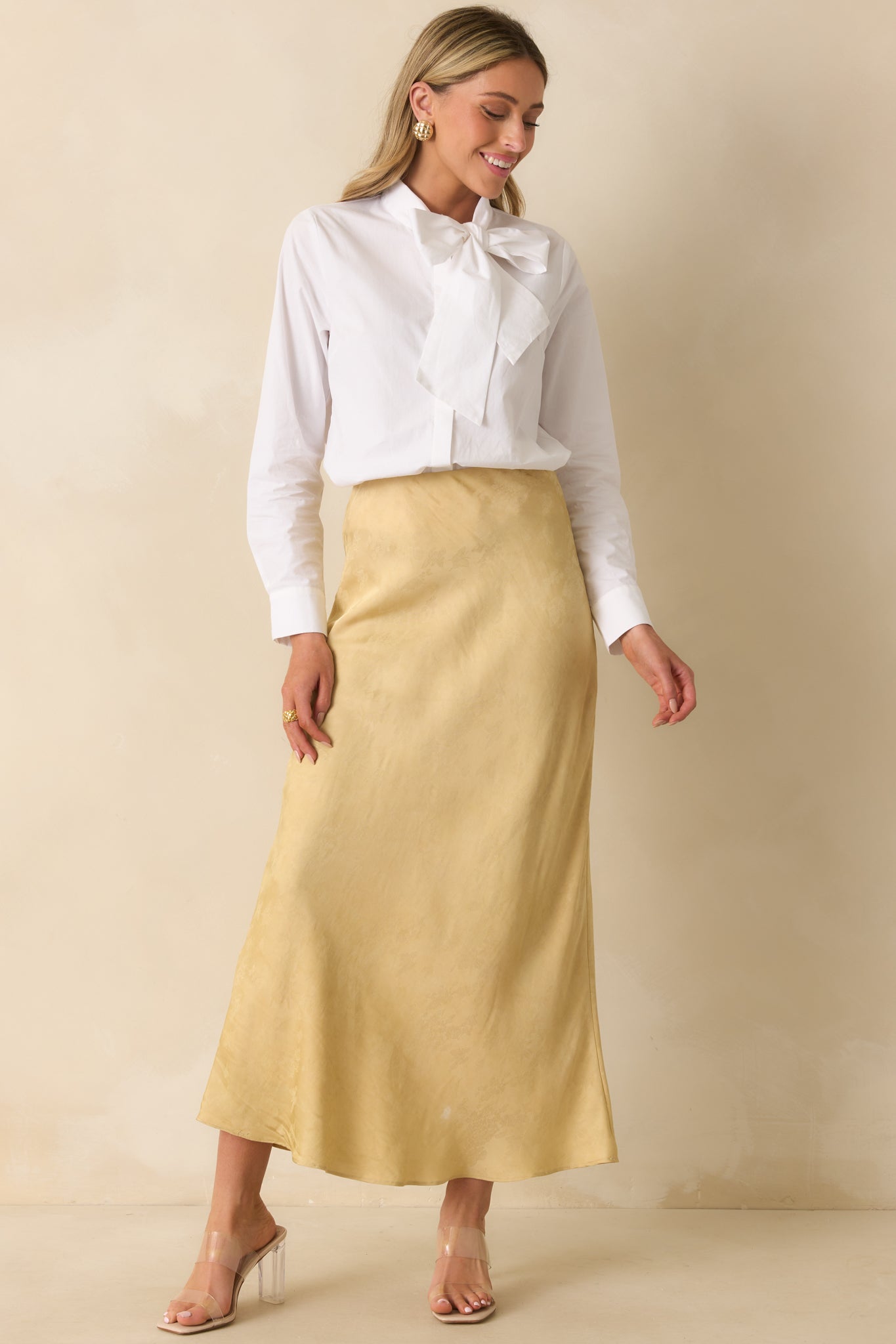 Full body of model wearing white top with a self-tie bow neckline and long sleeves with button cuffs.