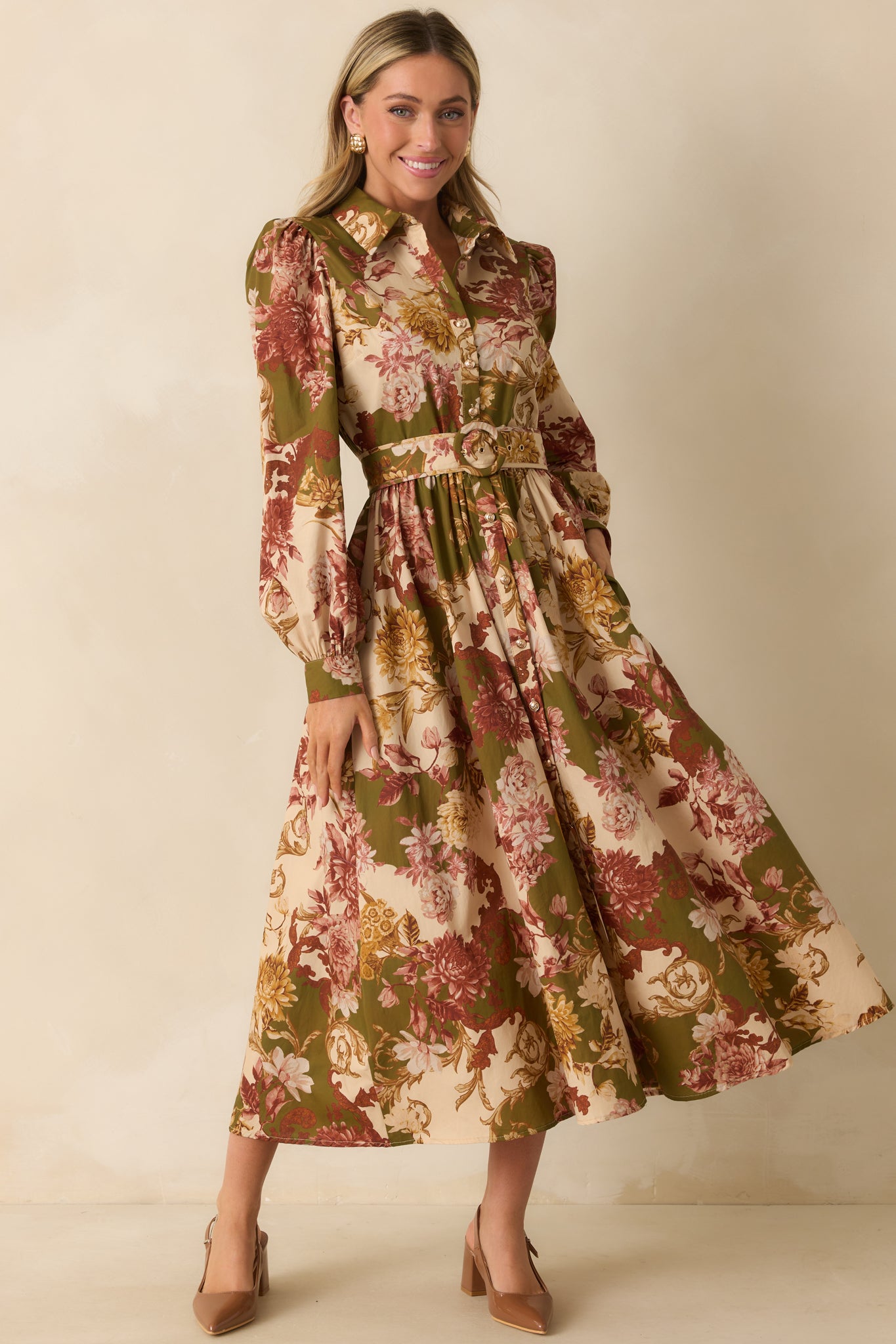 Front view of an olive green dress with a vibrant multicolor floral print, featuring a collared neckline, long puff sleeves with button cuffs, a button-down front, and an optional waist belt for shaping.