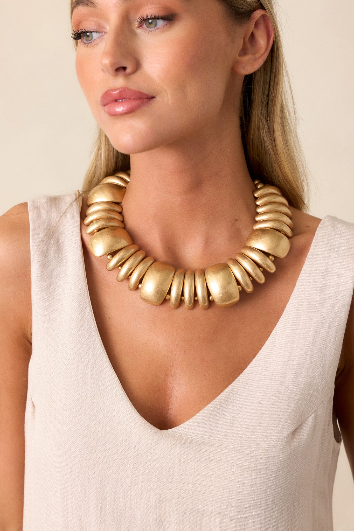 Full view of a gold necklace featuring a bold chunky design, gold hardware, metallic gold beads varying in size, a collar design and a lobster claw closure.