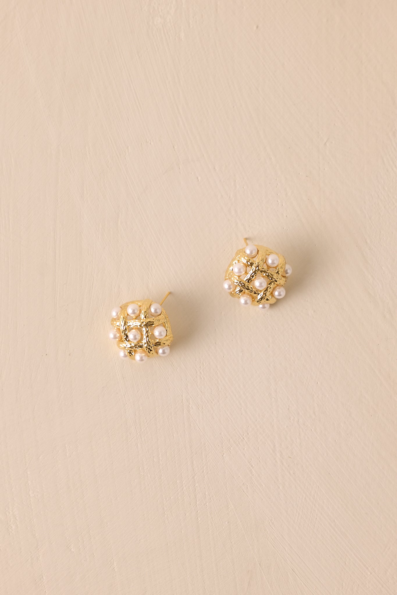 Front view of the gold woven earrings showing pearl accents and polished hardware on a neutral background.