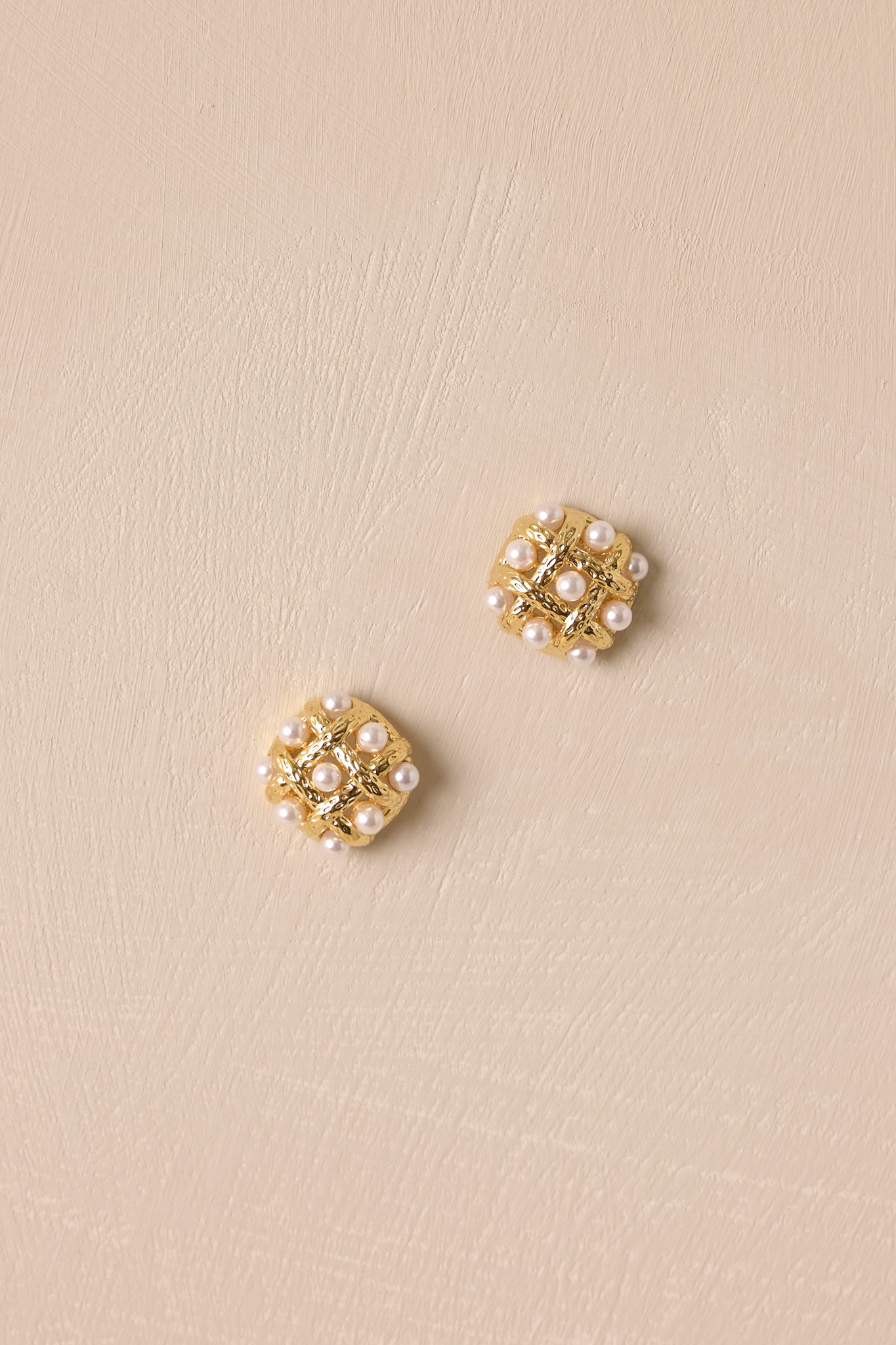 Pair of twisted gold weave earrings with pearls displayed against a beige background.