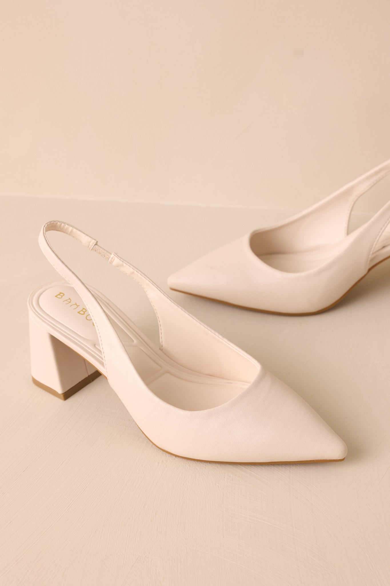 A cropped shot focusing on the pointed toe and strap detail of the ivory heels, showing the smooth faux leather material and sturdy block heel.
