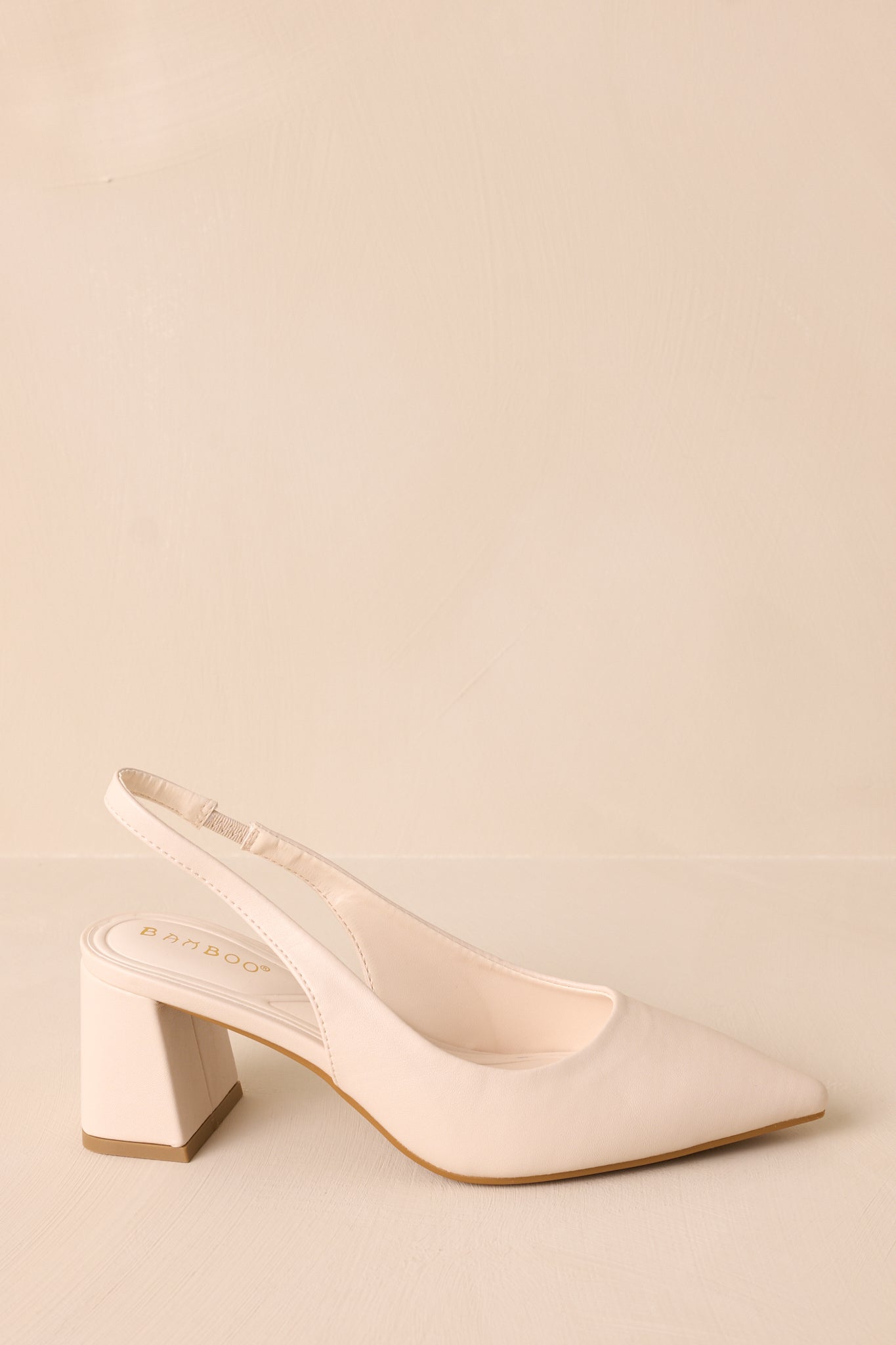 A side view of the ivory heels, featuring the pointed toe and thick block heel, with the faux leather material and strap around the back of the foot clearly visible.