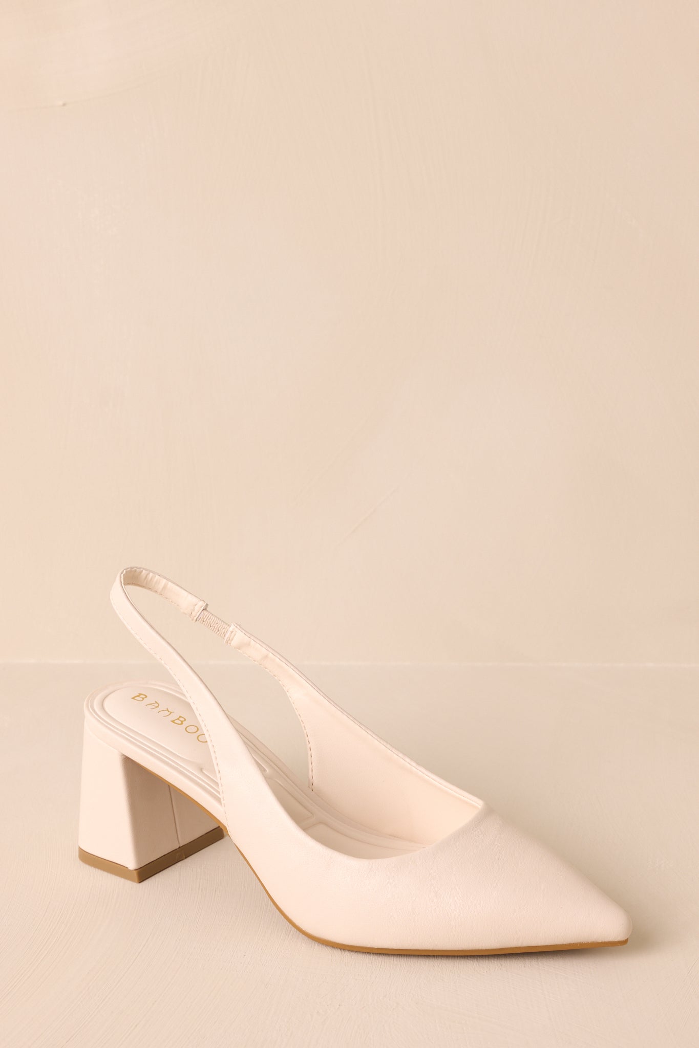 A diagonal angle showcasing the ivory heels from the front, highlighting the pointed toe, the strap around the back, and the solid block heel for a balanced look.
