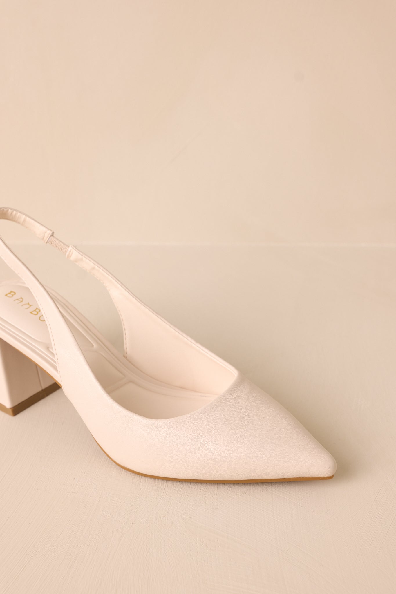 A detailed close-up of the ivory heels, focusing on the pointed toe, the strap around the back of the foot, and the block heel, highlighting the faux leather material and sturdy design.